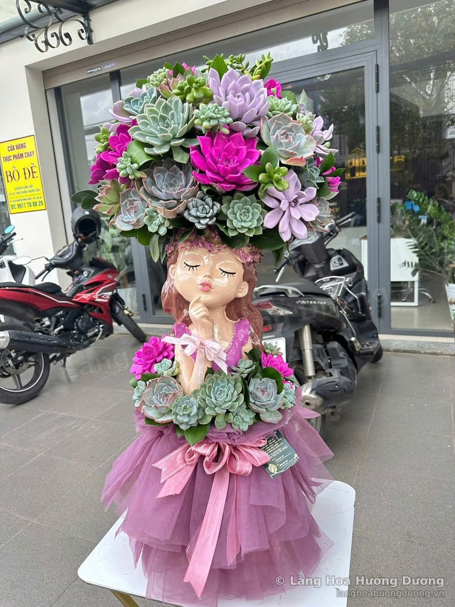 Chậu sen đá cô gái mặc váy voan hồng tím, đầu cắm sen đá tím xanh, đặt trước cửa kính